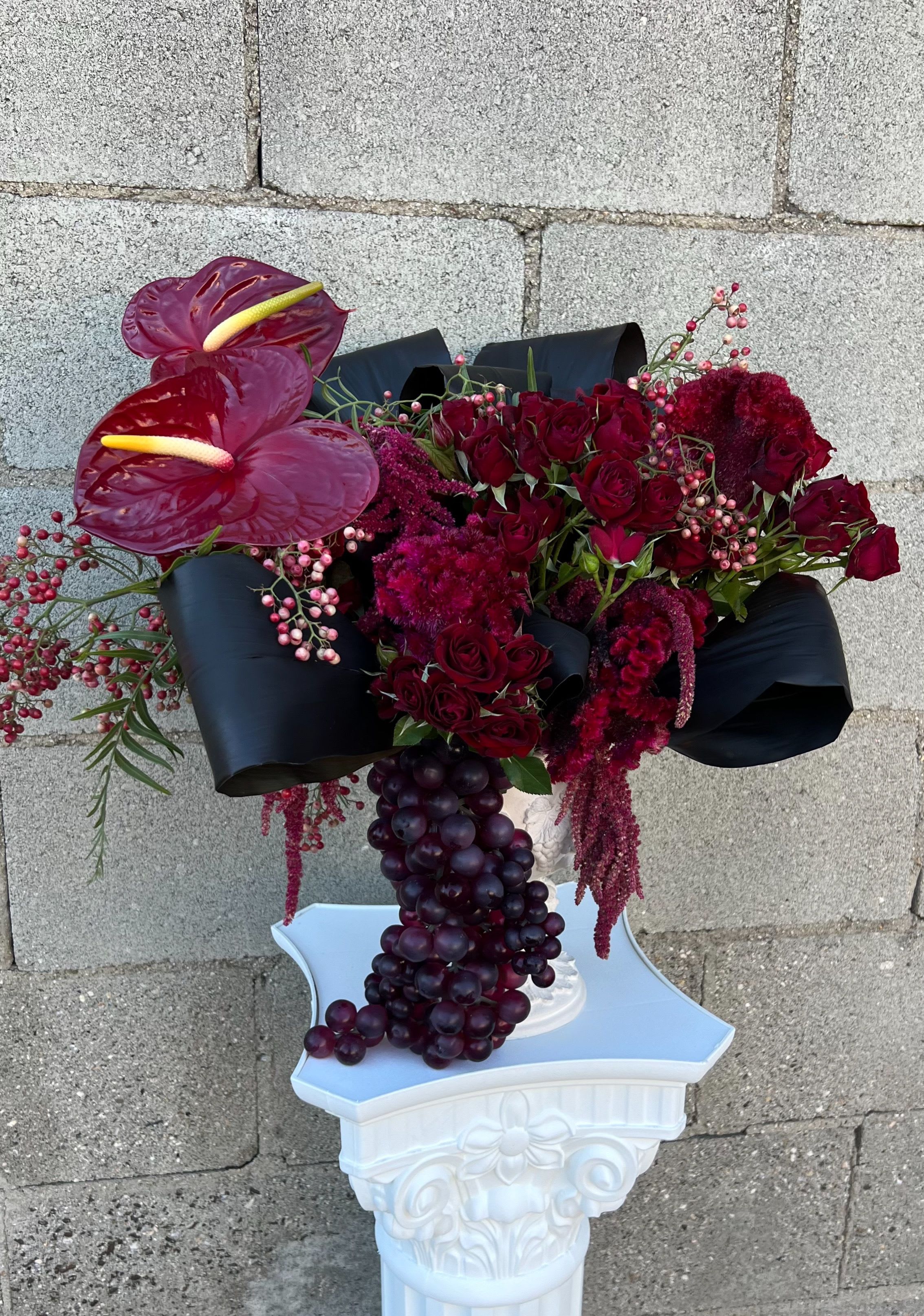 Deep red floral arrangement with anthuriums and roses in a white pedestal vase