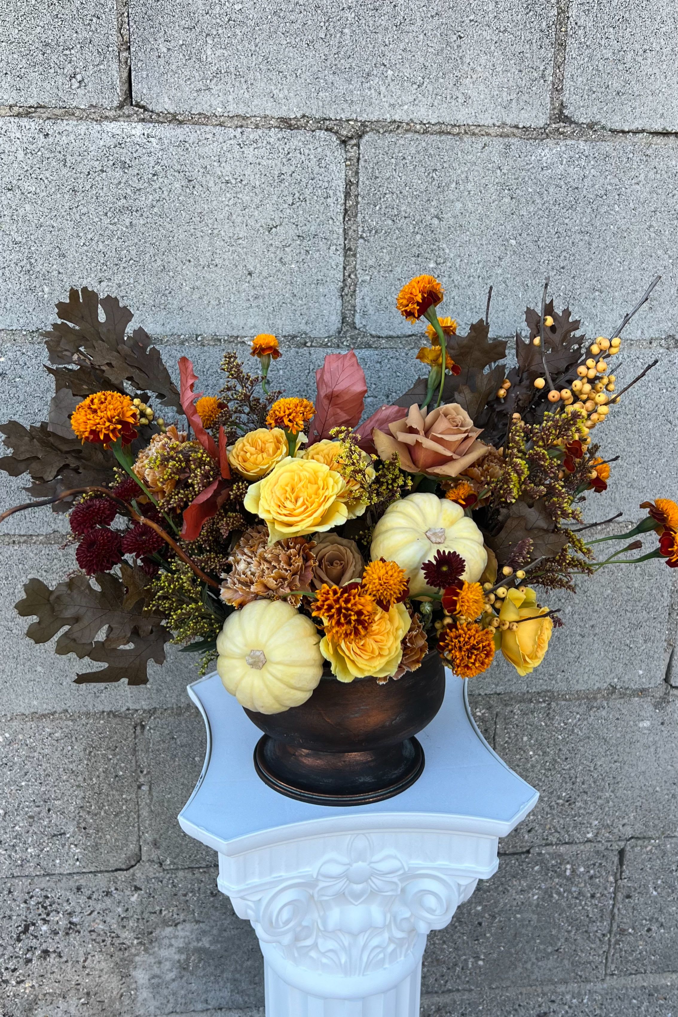 Autumn floral arrangement with yellow roses, marigolds, and small pumpkins in a dark vase