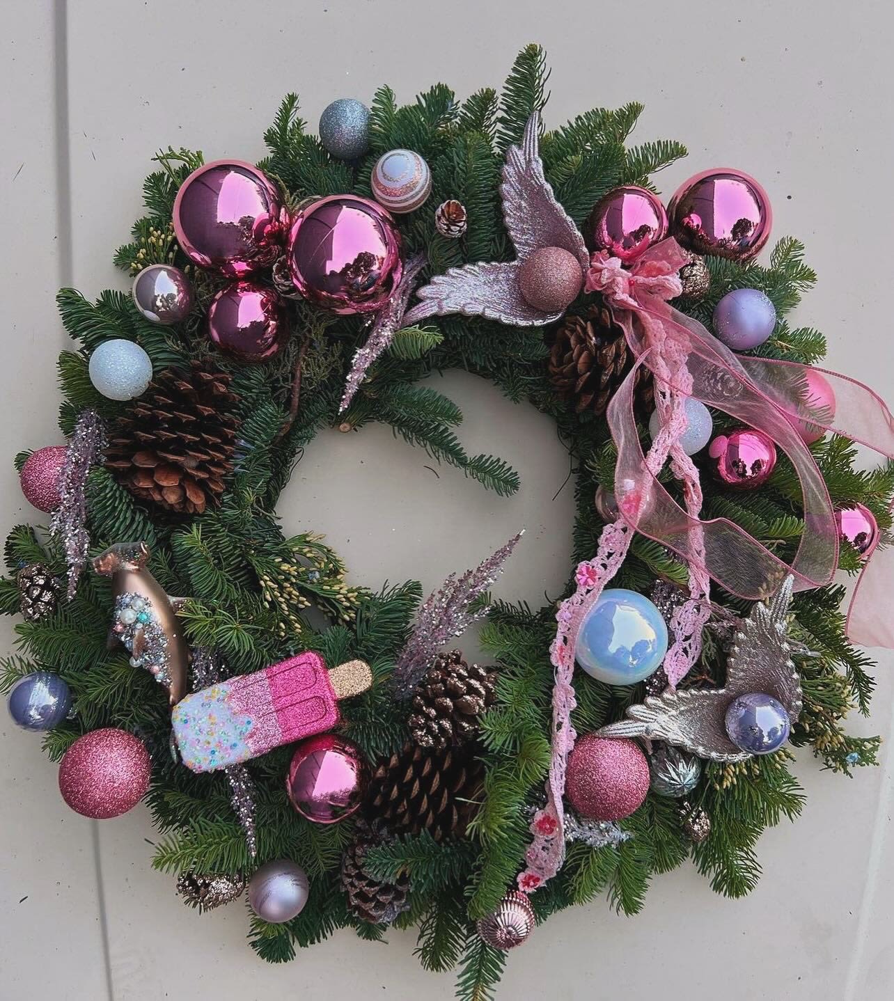 Christmas wreath with pink ornaments, pinecones, and ribbon