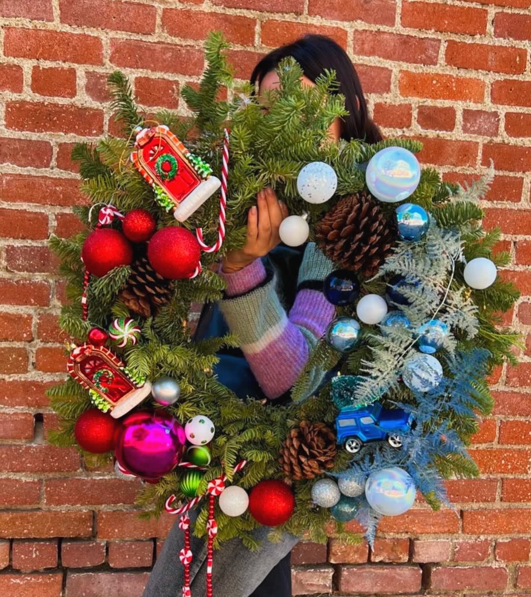 Person holding a decorated Christmas wreath with ornaments and pinecones
