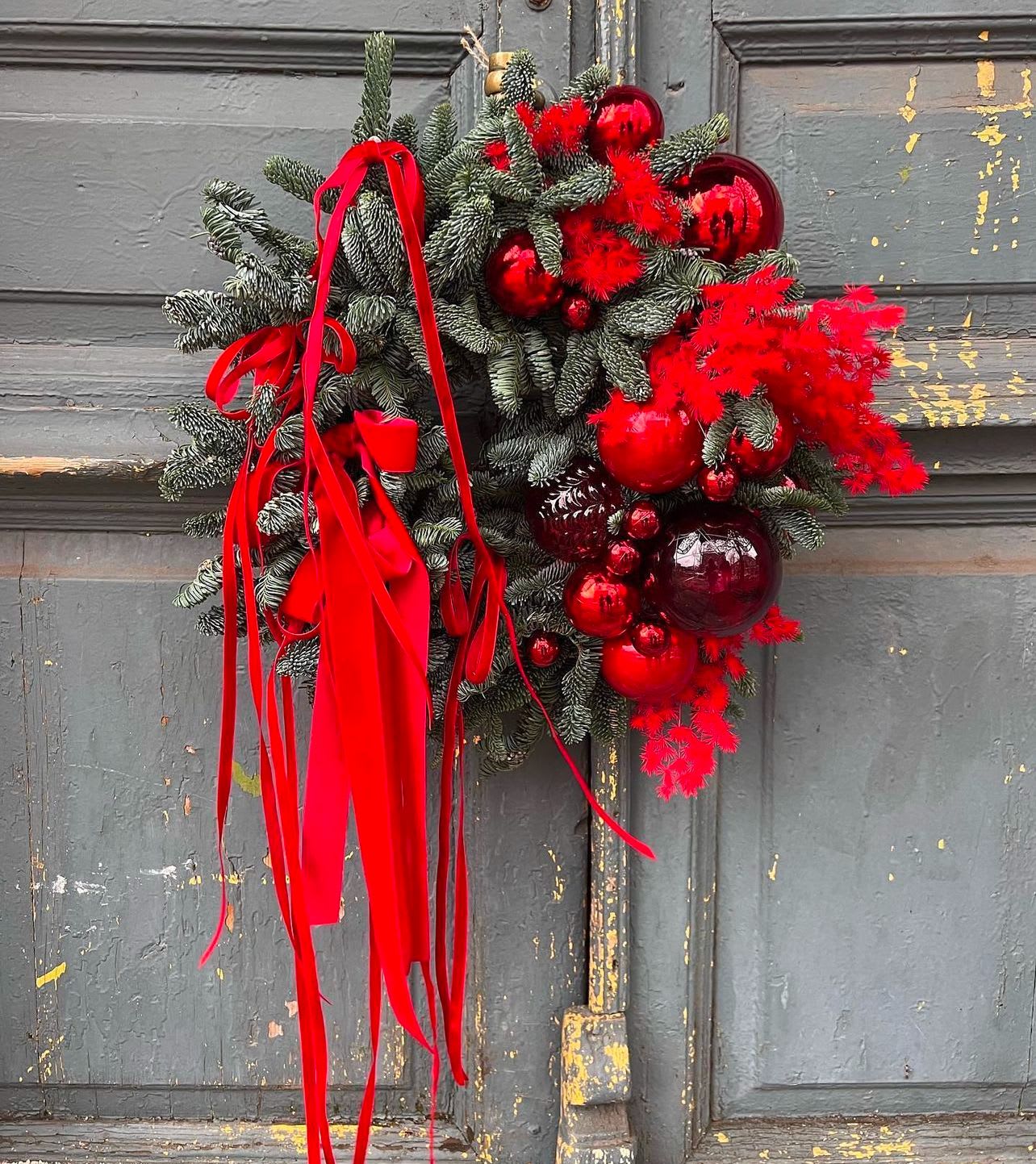 Holiday wreath with red ornaments and ribbon on a gray door