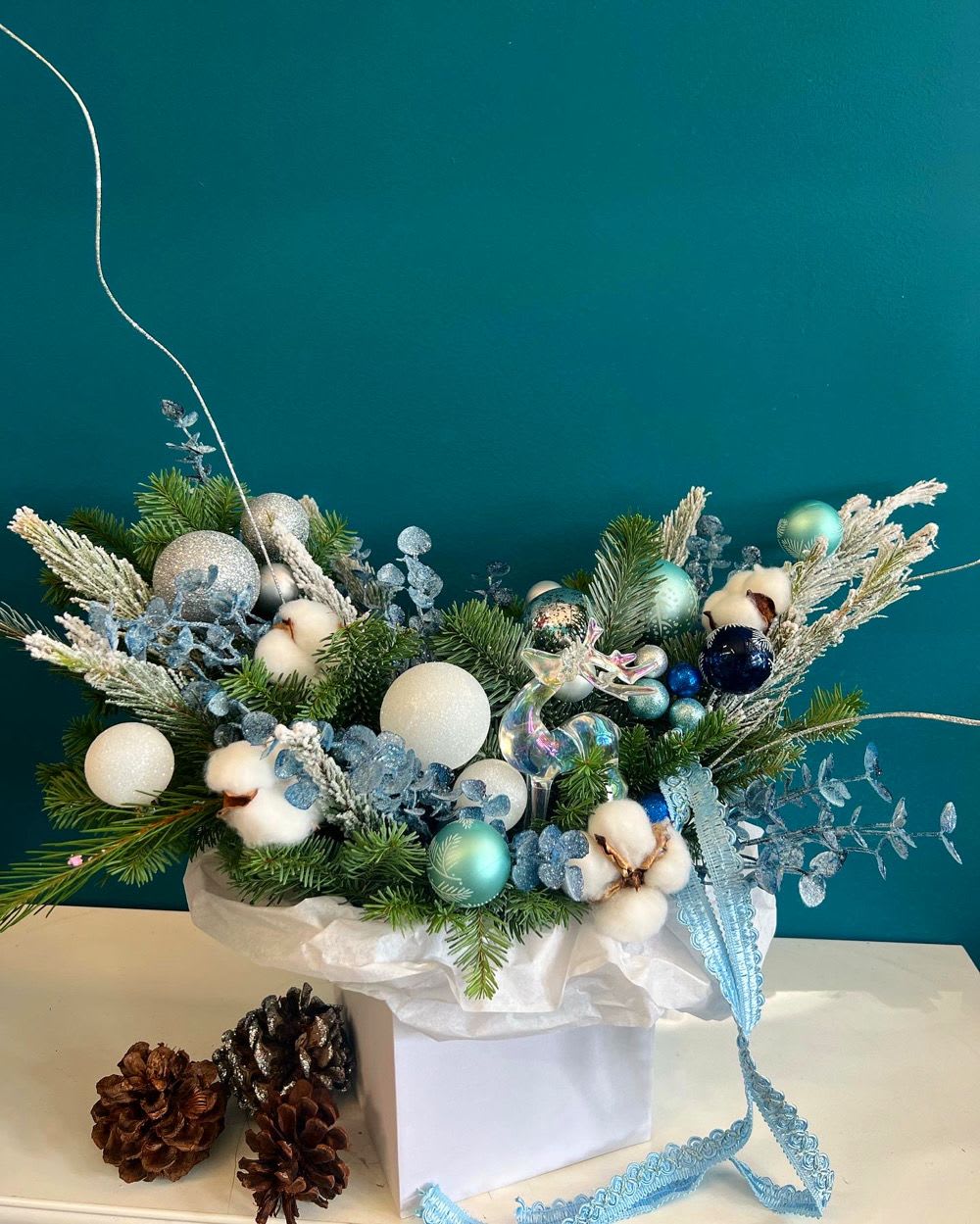 Holiday arrangement with pine, cotton bolls, and blue ornaments in a white box