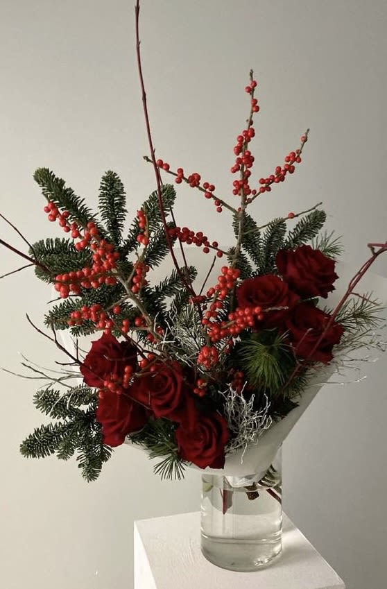 Red roses and berry branches in a clear glass vase