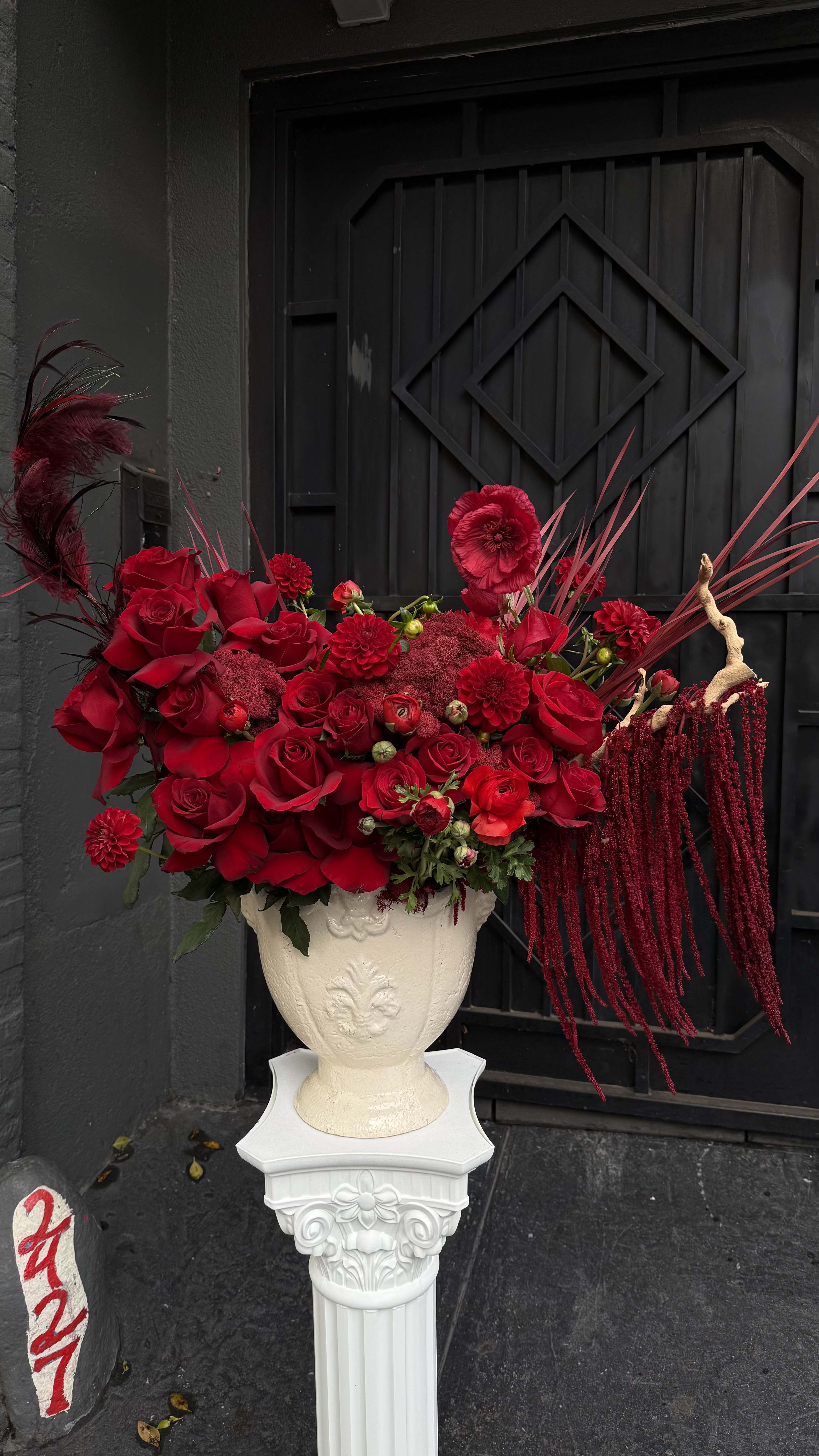 Red floral arrangement in a white pedestal vase