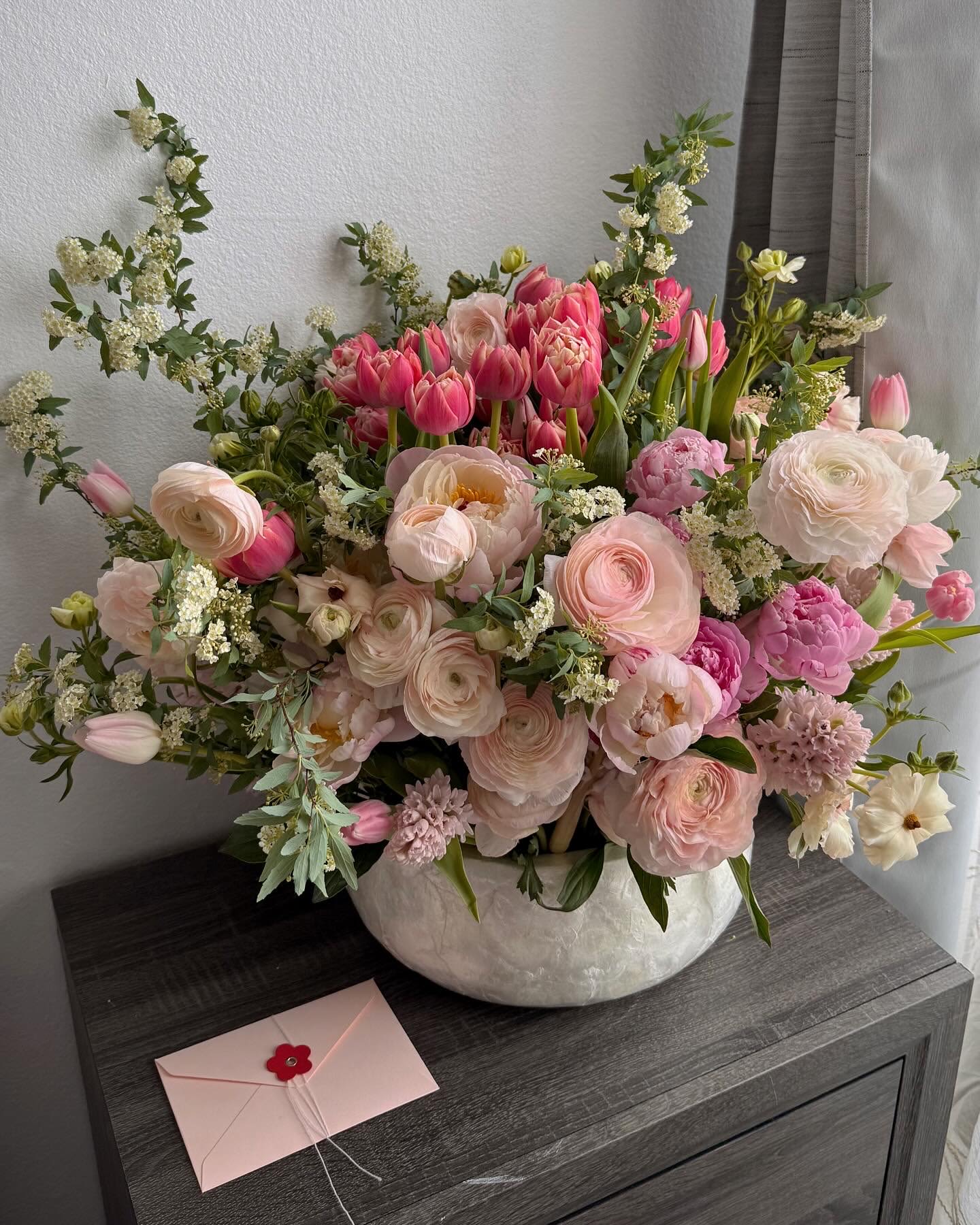 Pink and white mixed flower arrangement in a ceramic bowl with a card