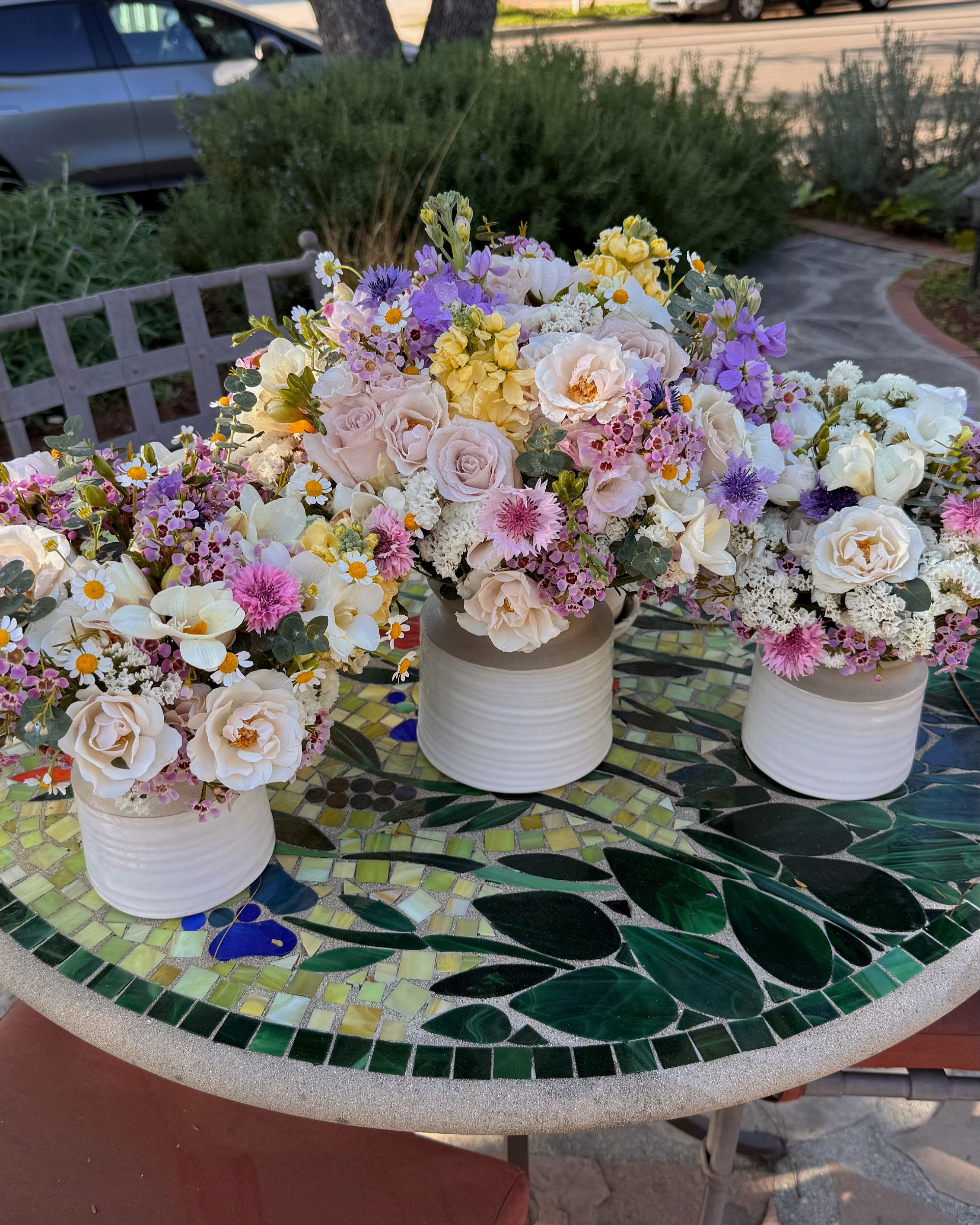 Three pastel floral centerpieces in white ceramic vases on a mosaic table