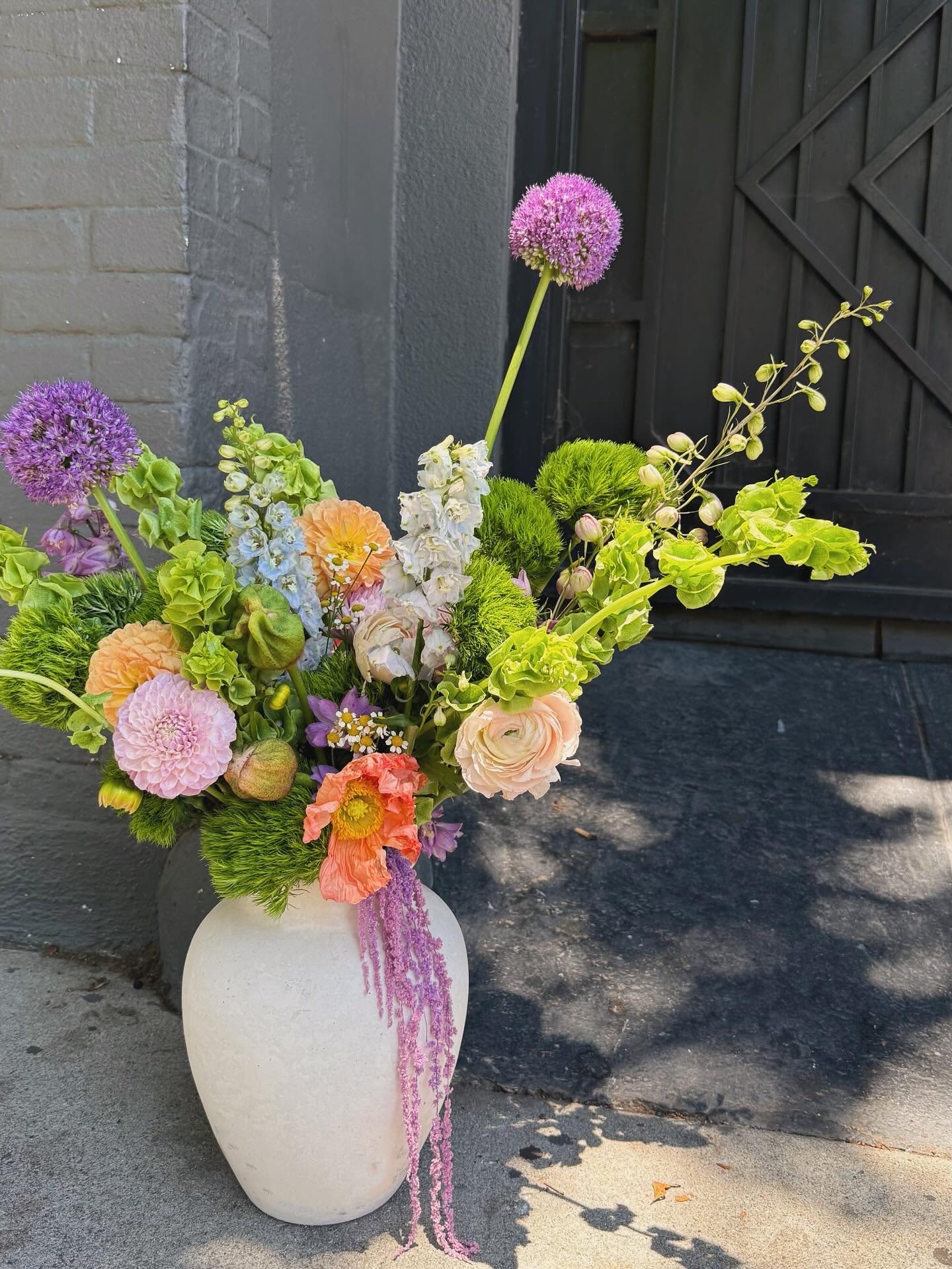 Large mixed floral arrangement in a white vase with purple, peach, and green blooms