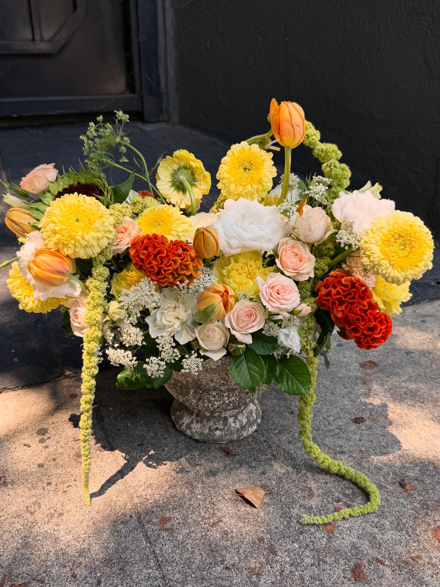 Mixed bouquet in a stone urn with yellow, peach, white, and orange blooms