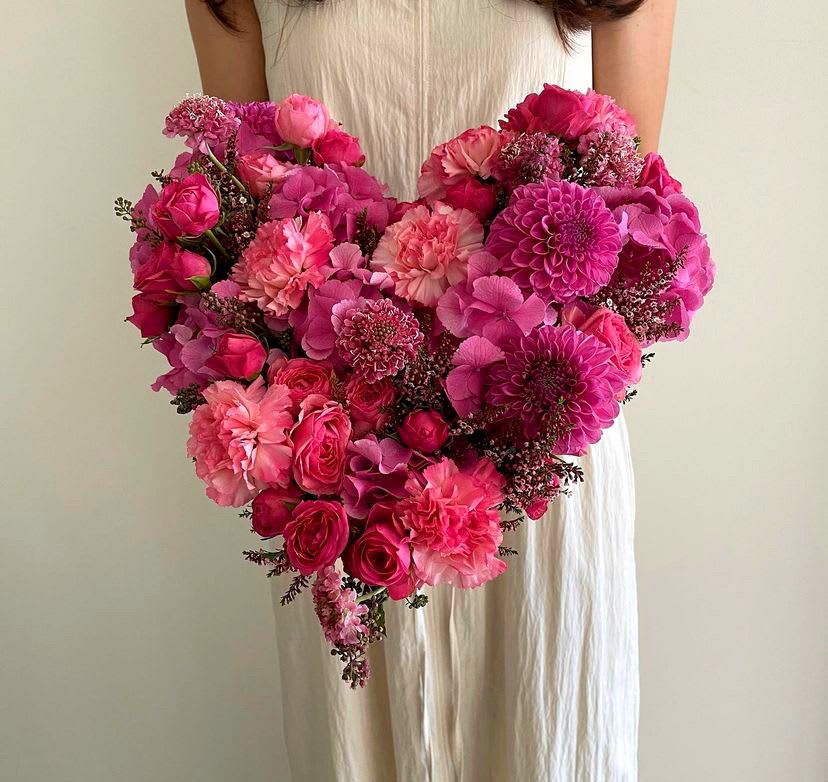 Heart-shaped bouquet of pink flowers held by a person in a white dress
