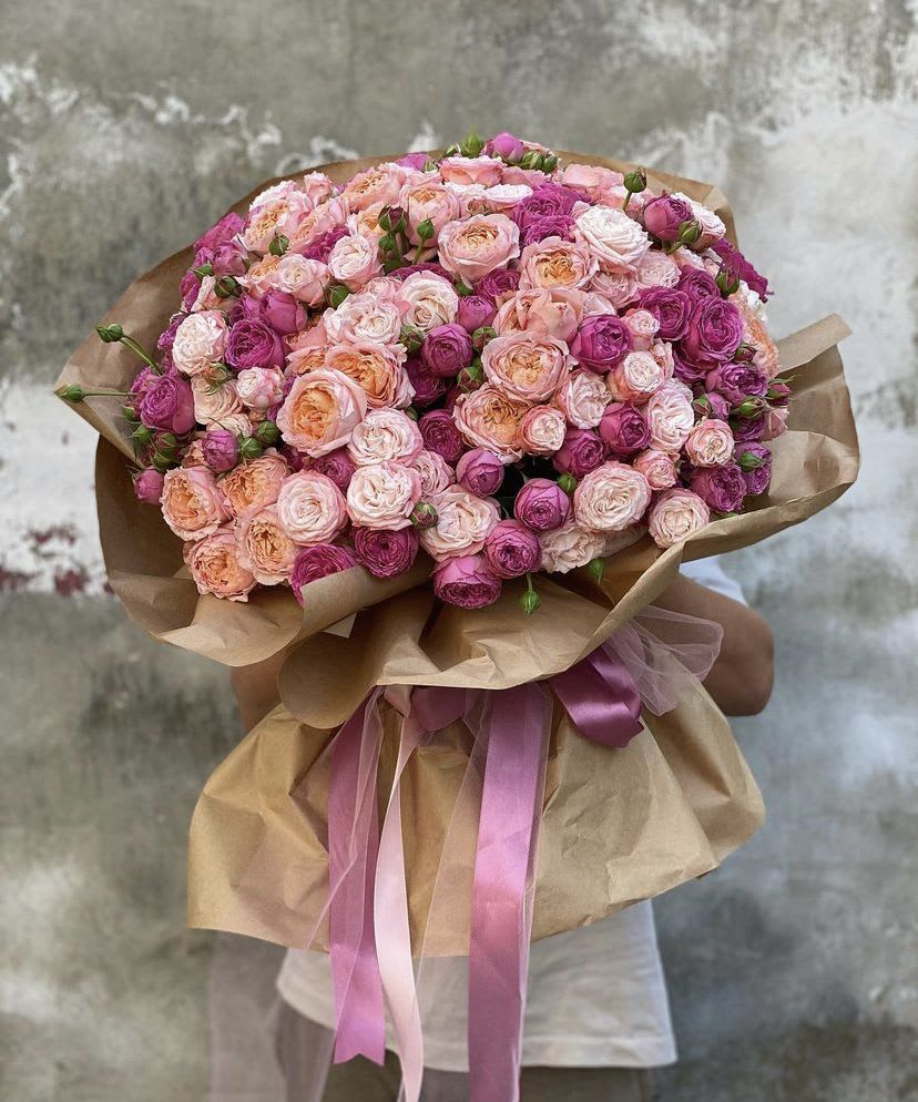 Large bouquet of pink and peach roses wrapped in brown paper with pink ribbons