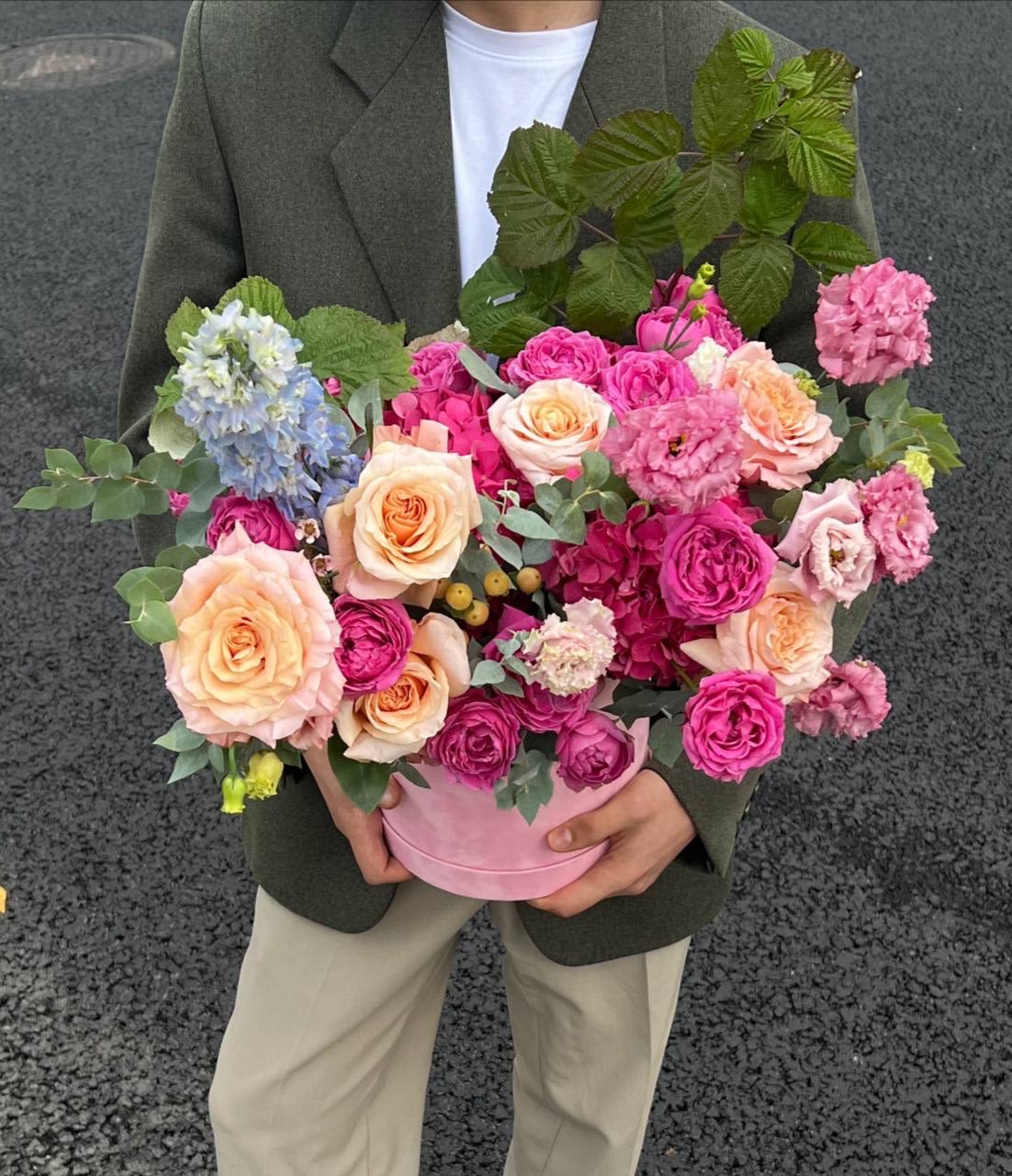 Pink and peach roses arranged in a round pink box with blue blooms