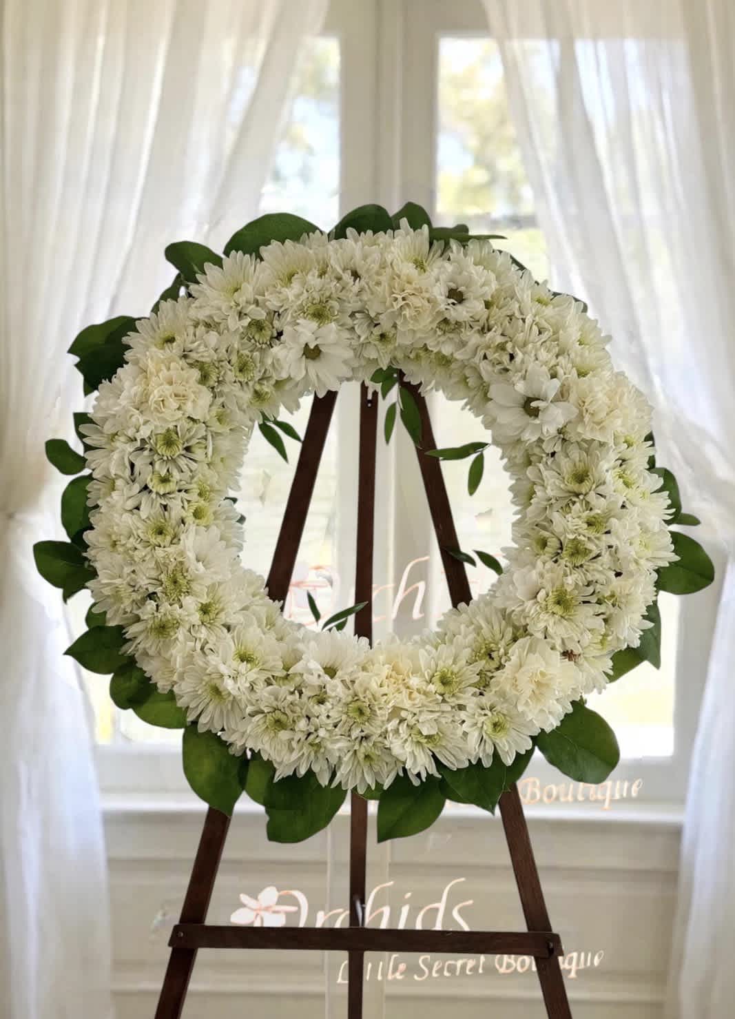 White flower wreath on a wooden easel with green leaves