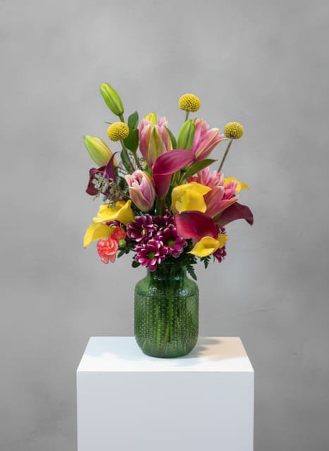 Colorful bouquet of lilies, calla lilies, and mums in a green glass vase