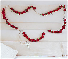 Red rose garland draped on a white upholstered headboard with a rosary cross