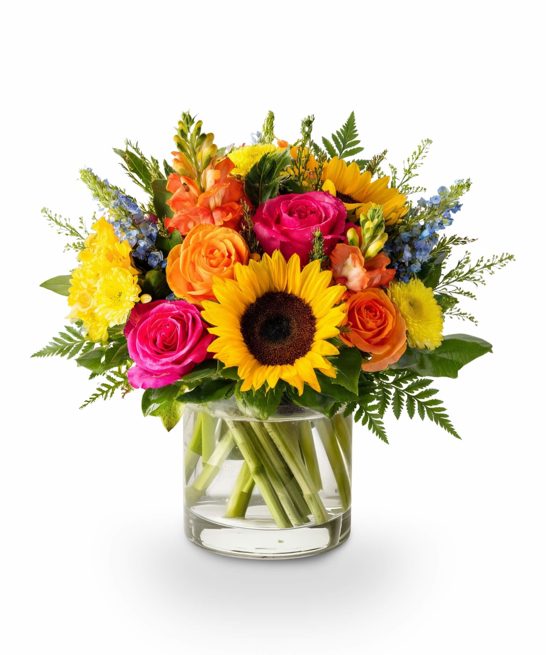 Sunshine Fiesta - Let summer burst into bloom with Sunshine Fiesta — a dazzling celebration of bright pinks, golden yellows, and vivid oranges. Sunflowers anchor this cheerful arrangement with bold, sunny energy, while hot pink and orange roses add vibrant pops of color. Soft orange snapdragons and yellow chrysanthemums complete the palette, bringing texture and warmth to every angle. Designed in a clear glass vase, this joyful bouquet feels like sunshine in floral form — a radiant pick for summer birthdays, garden parties, or simply brightening someone's day.