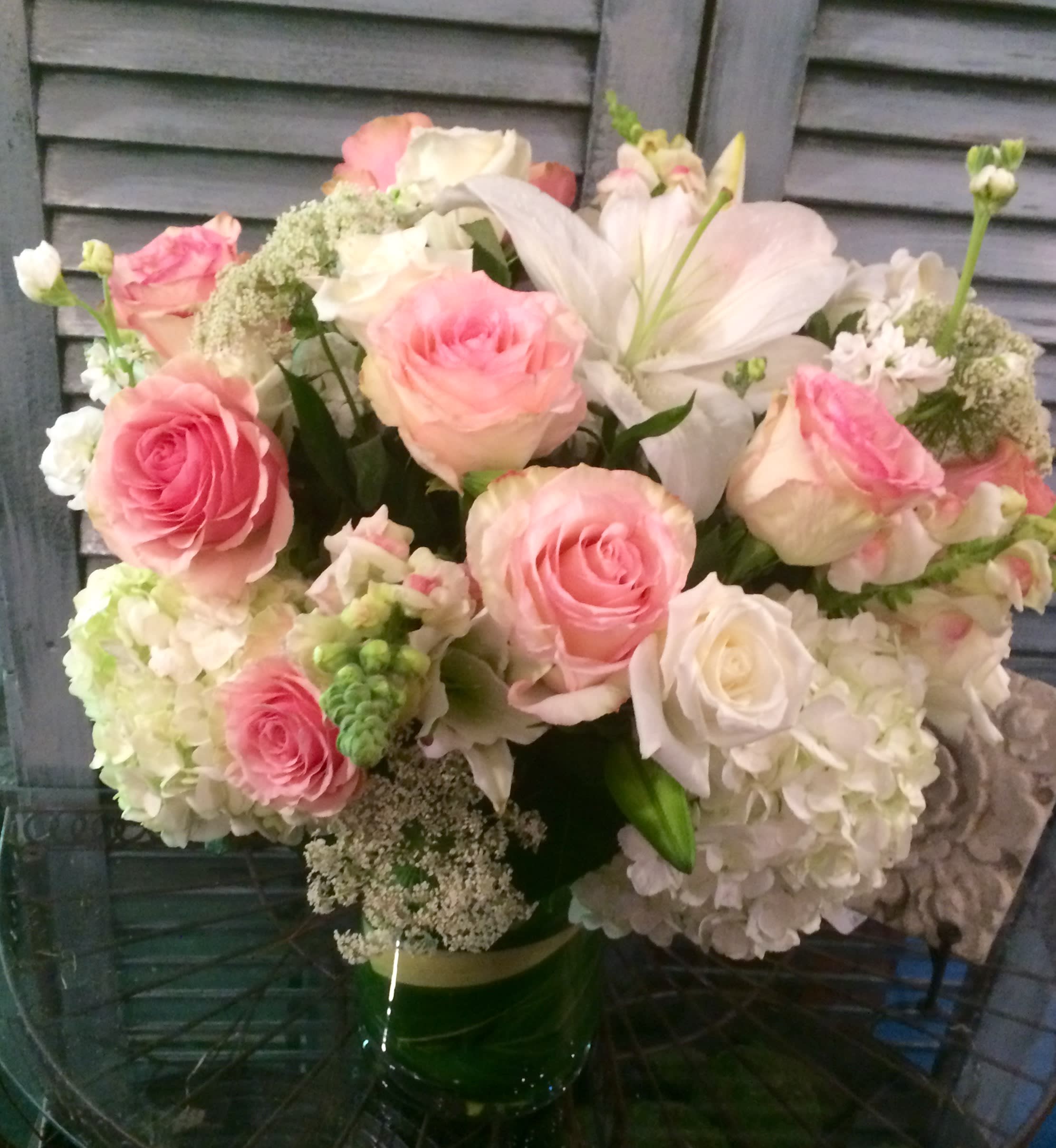 Round arrangement of pink roses, white lilies and white hydrangeas in a clear glass vase
