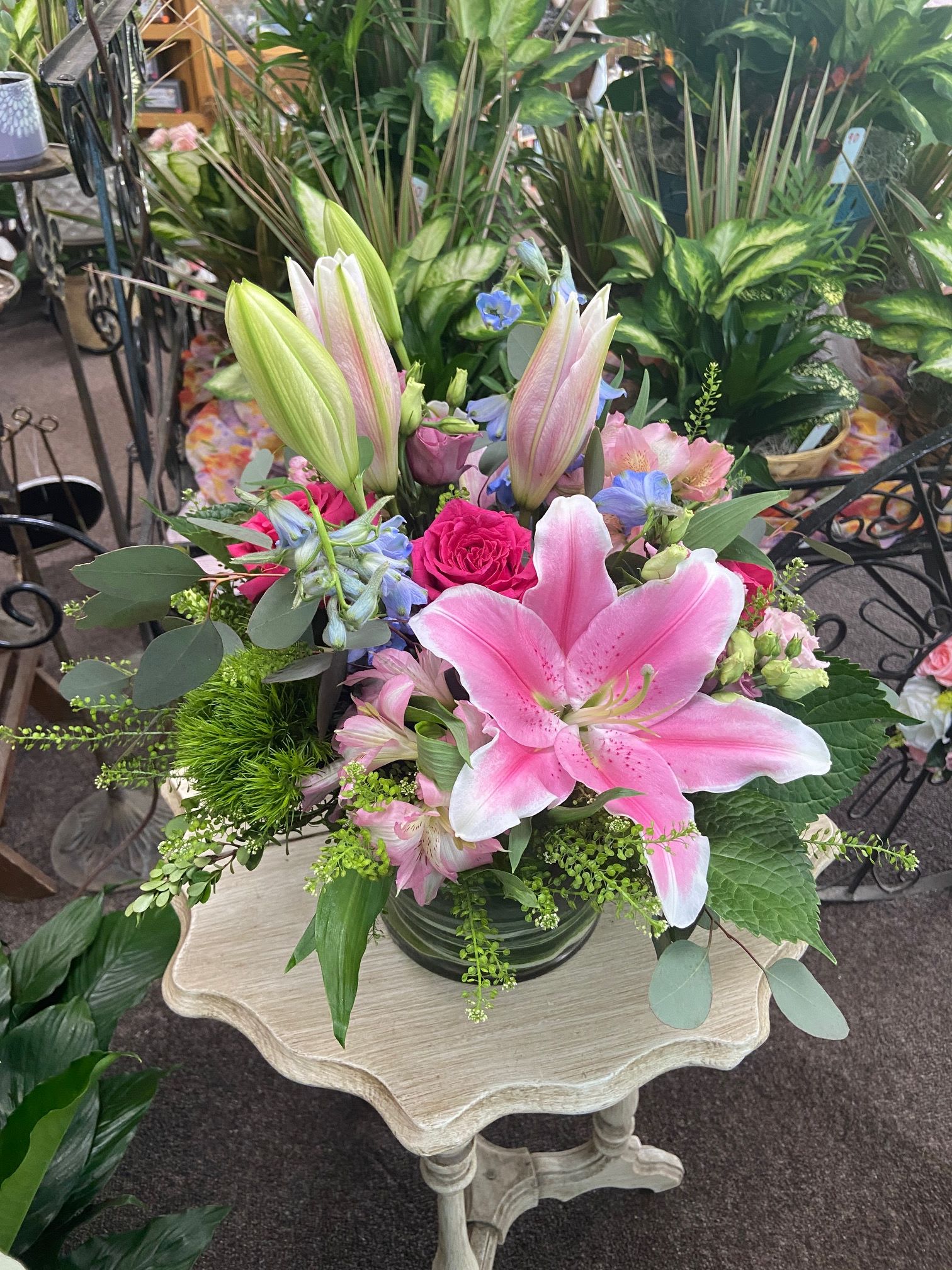Mixed bouquet of pink lilies, roses, and accent blooms in a clear glass vase on a small wooden table