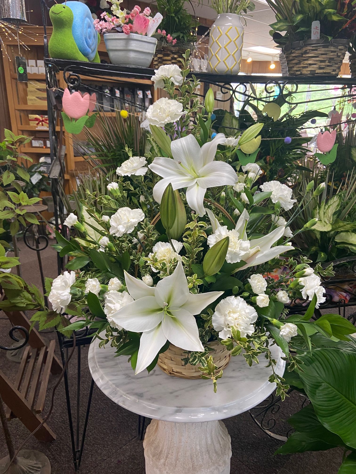 White lilies and carnations arranged in a woven basket on a small marble pedestal table