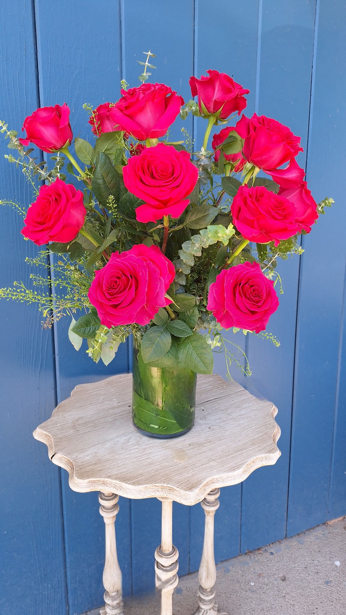 Tall arrangement of bright pink roses in a clear glass vase on a small wooden table.