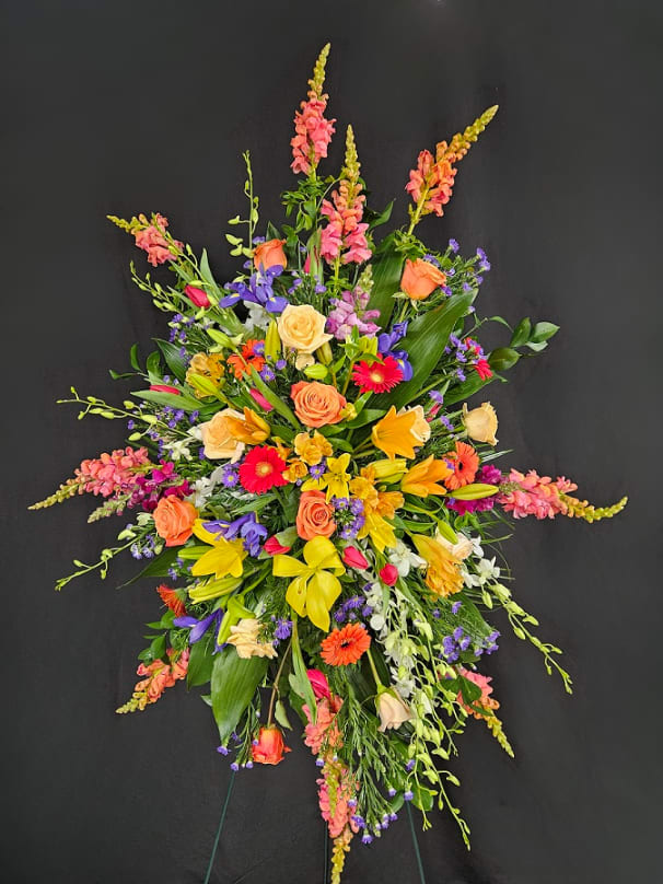 Tall standing spray of yellow lilies, orange roses, and bright mixed flowers on a black background