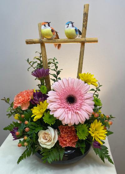 Colorful flower arrangement with two decorative birds on a bamboo frame