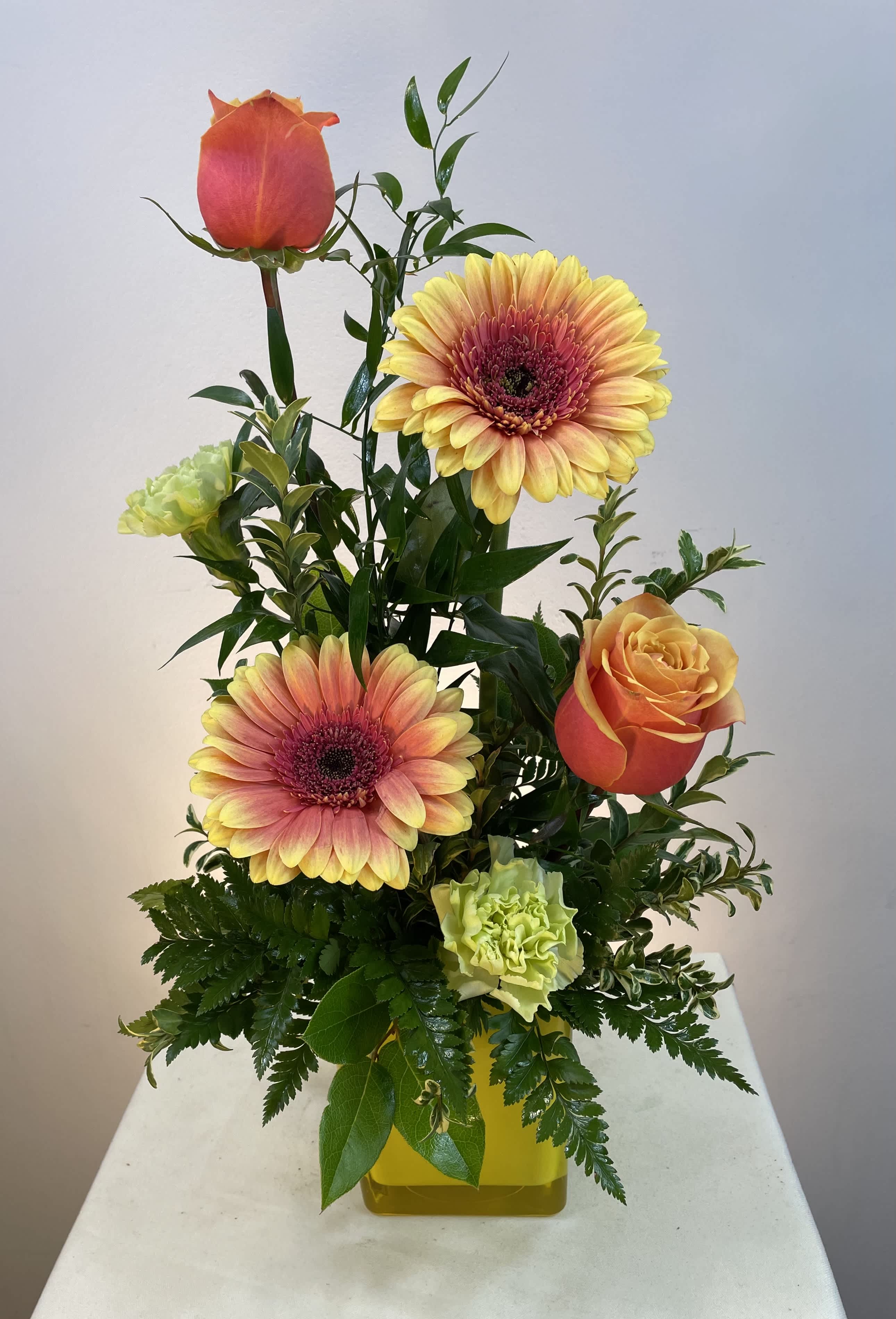 Mixed bouquet with orange roses, pink-yellow gerbera daisies, and green carnations in a yellow vase