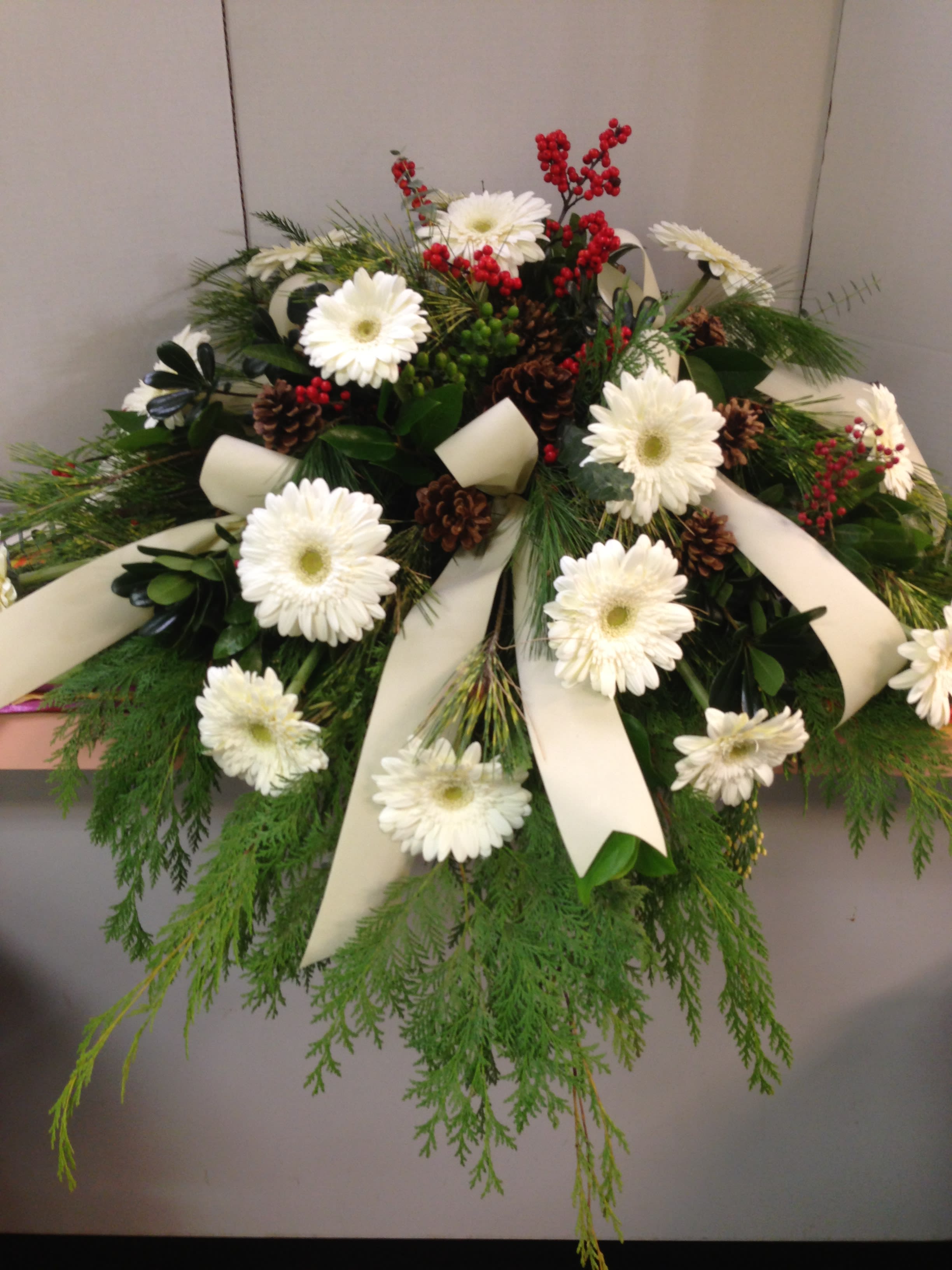 White gerbera daisies with red berries and cream ribbons in a low arrangement