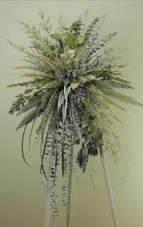 Tall standing arrangement of cascading mixed greenery on a pale backdrop