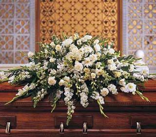 Large white floral casket spray arranged on a polished wooden coffin
