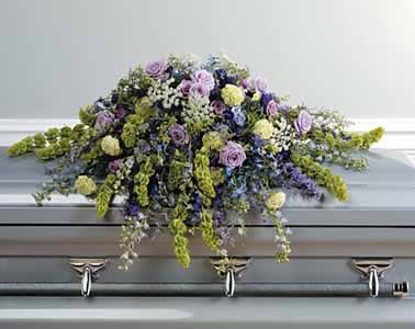 Pastel casket spray of lavender, yellow, blue, and green flowers on a silver casket
