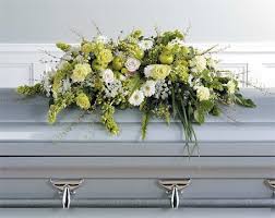 Long white and green flower casket spray arranged on top of a light gray casket.