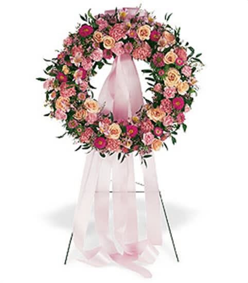 Standing wreath of pink and peach flowers with long pink ribbons on a metal easel