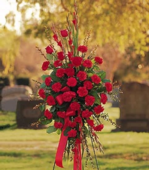 Standing spray of red carnations with ribbon on an easel in a cemetery setting