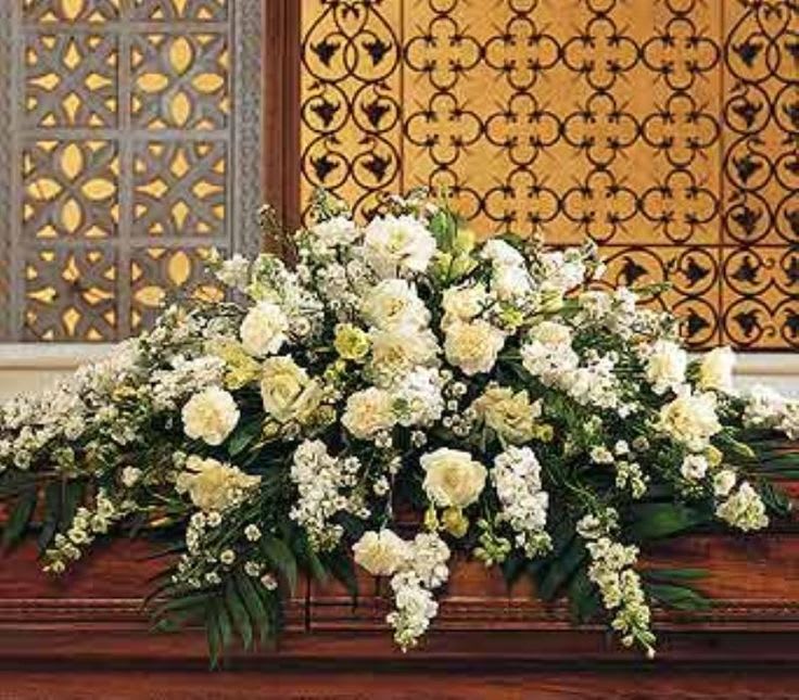Large white and cream floral casket spray arranged in a low, elongated shape