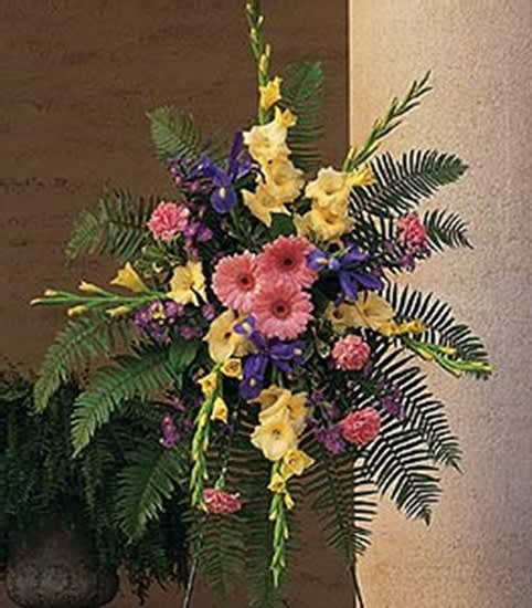 Tall standing spray with pink gerbera daisies, yellow blooms and purple irises in a fan-shaped design