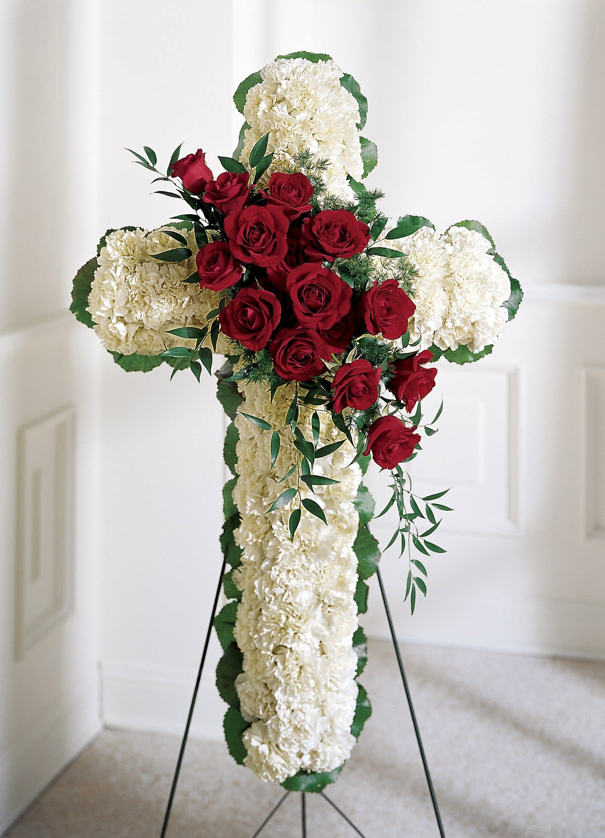 Standing cross of white carnations with a cluster of red roses on an easel