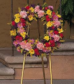 Standing wreath of mixed pink, yellow, red, and purple flowers on a gold easel.