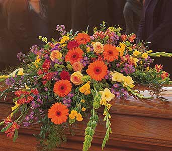 Bright mixed casket spray with orange gerberas and yellow roses on a wooden casket