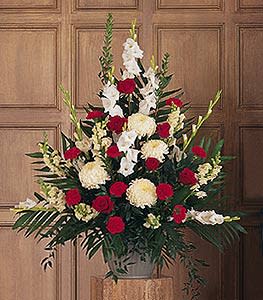 Tall arrangement of red roses, white gladiolus, and cream flowers in an urn-style vase.
