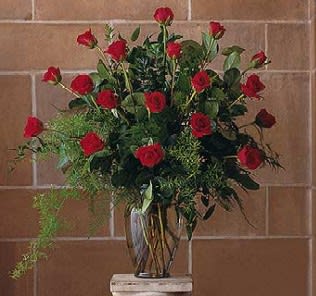 Tall arrangement of red roses with trailing greenery in a clear glass vase