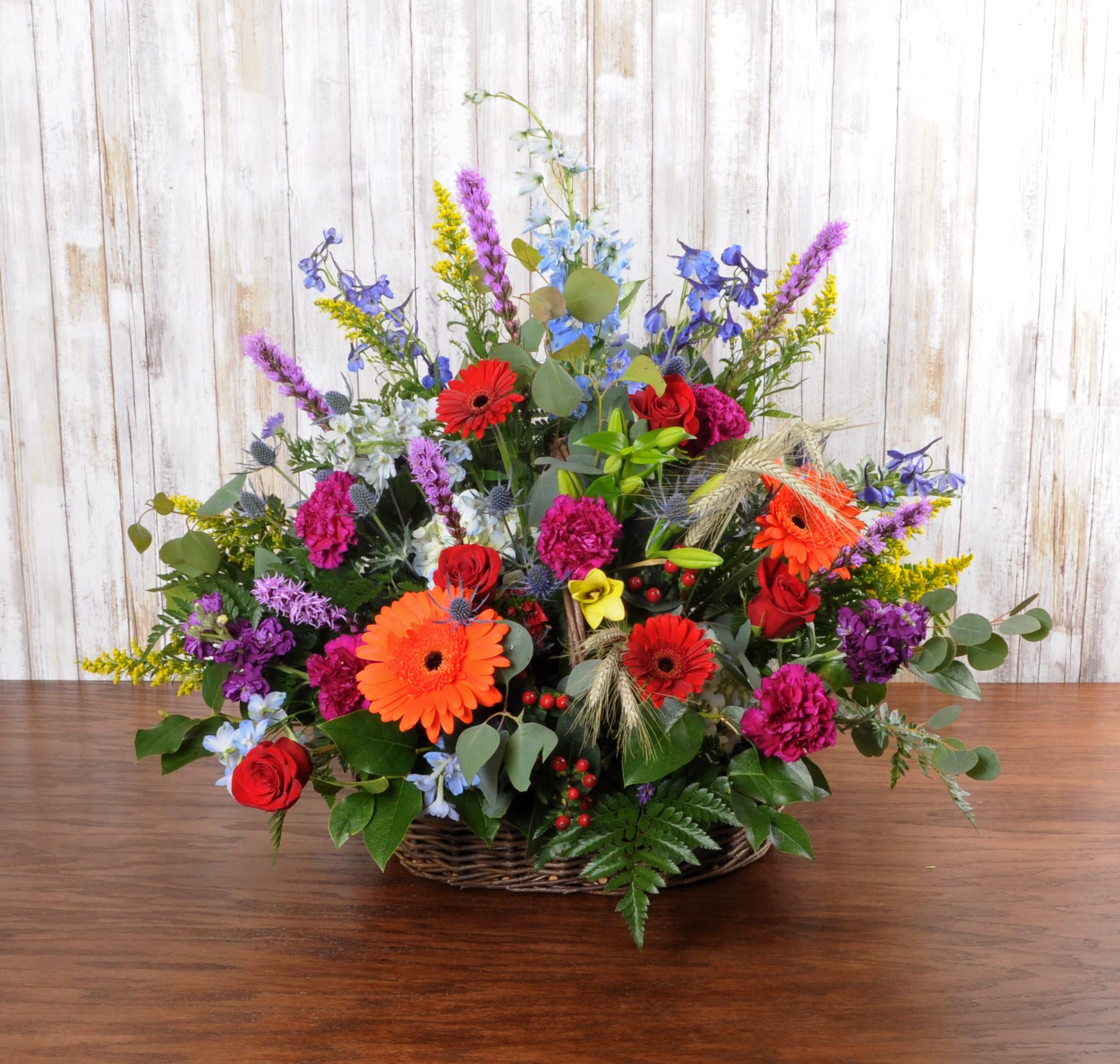 Colorful mixed flower arrangement with red roses and orange gerberas in a wicker basket.