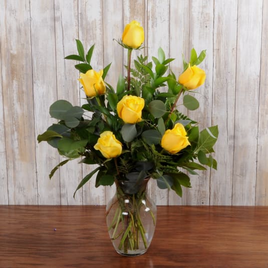 Tall arrangement of yellow roses in a clear glass vase on a wooden surface