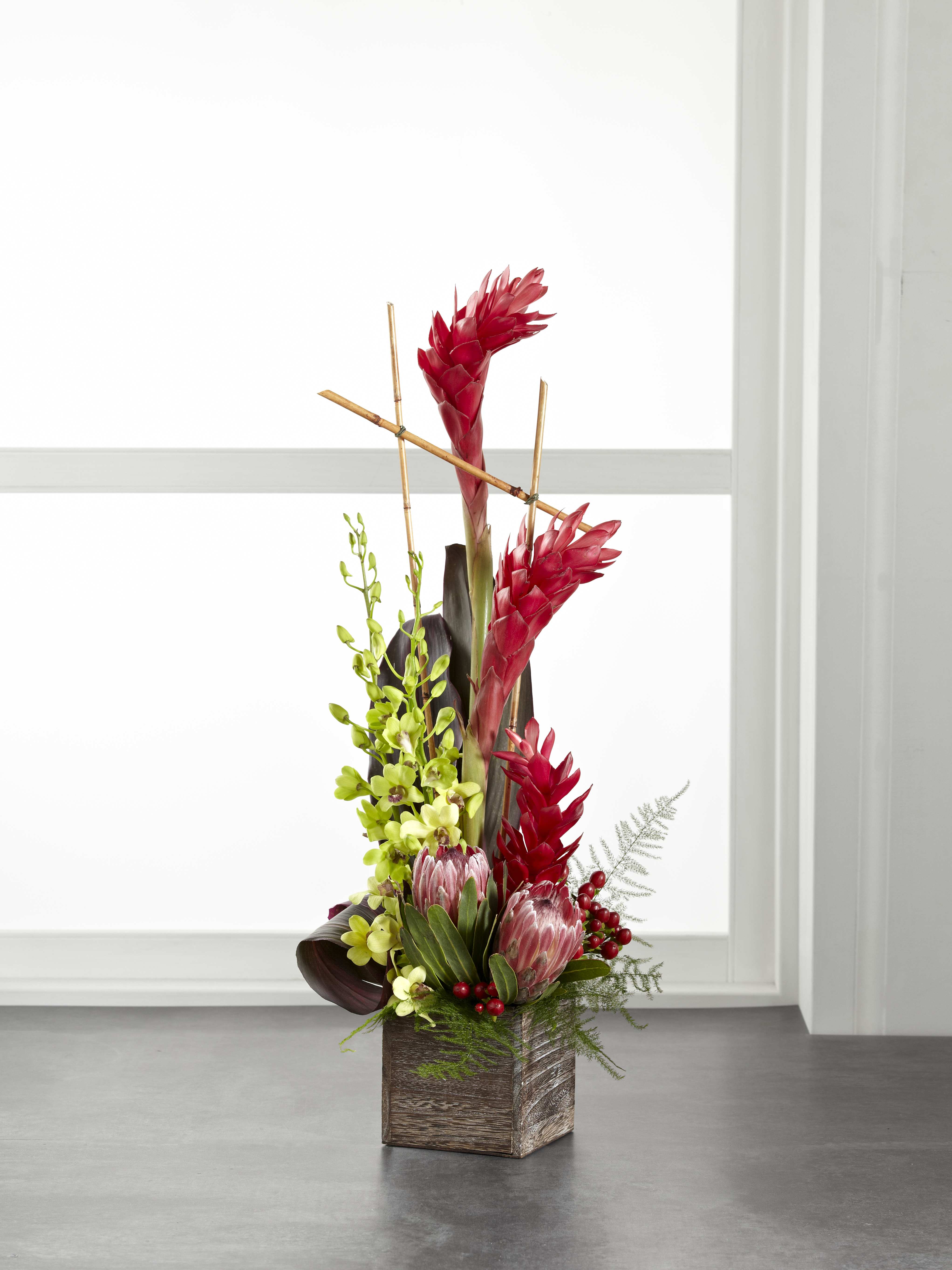 Tall tropical arrangement with red blooms in a wooden cube vase
