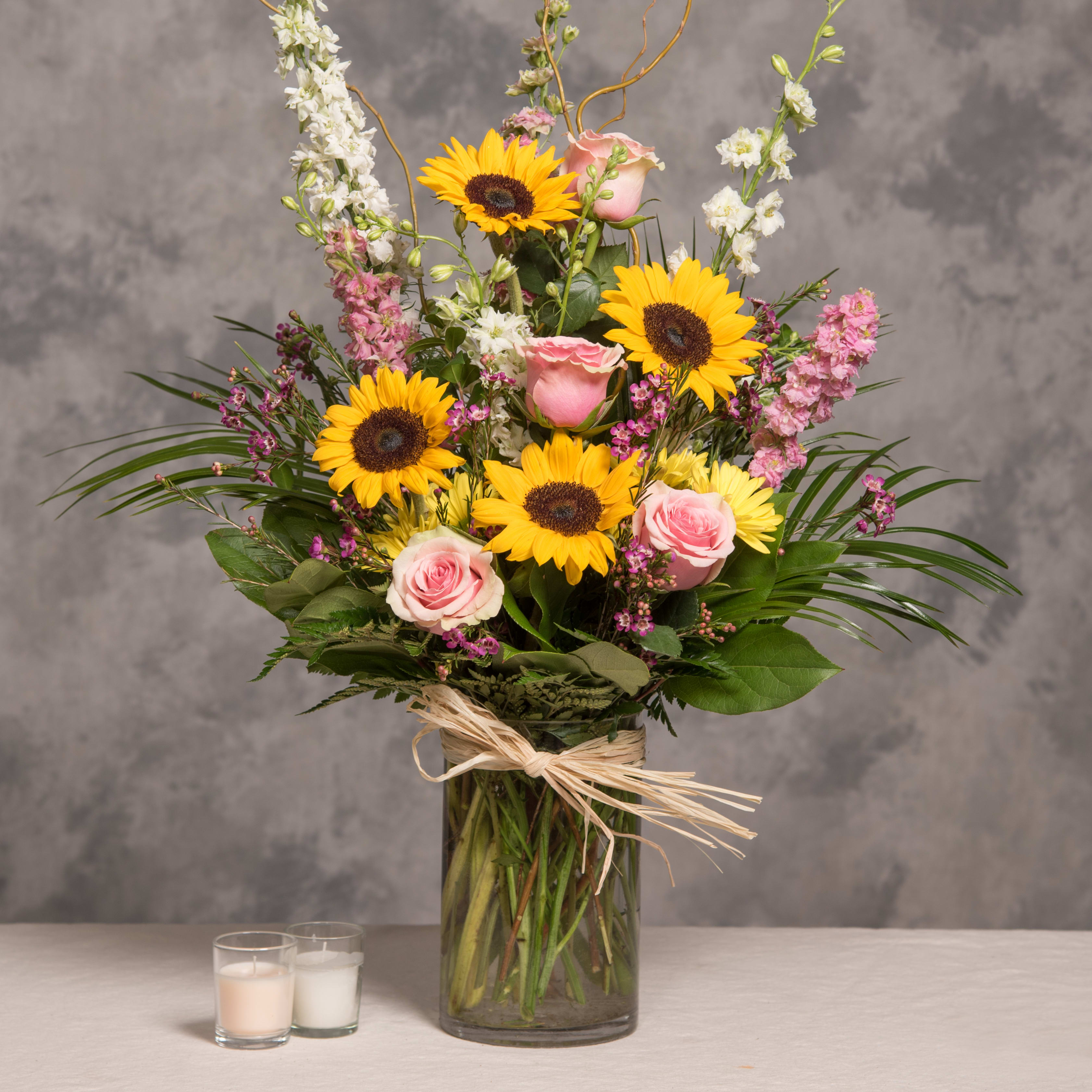Bouquet of sunflowers and pink roses in a glass vase with candles nearby