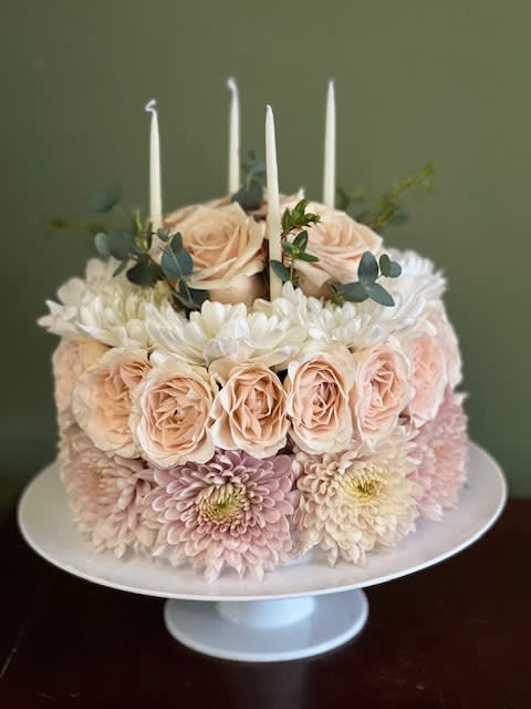 Round floral cake with pale roses, chrysanthemums, and white candles