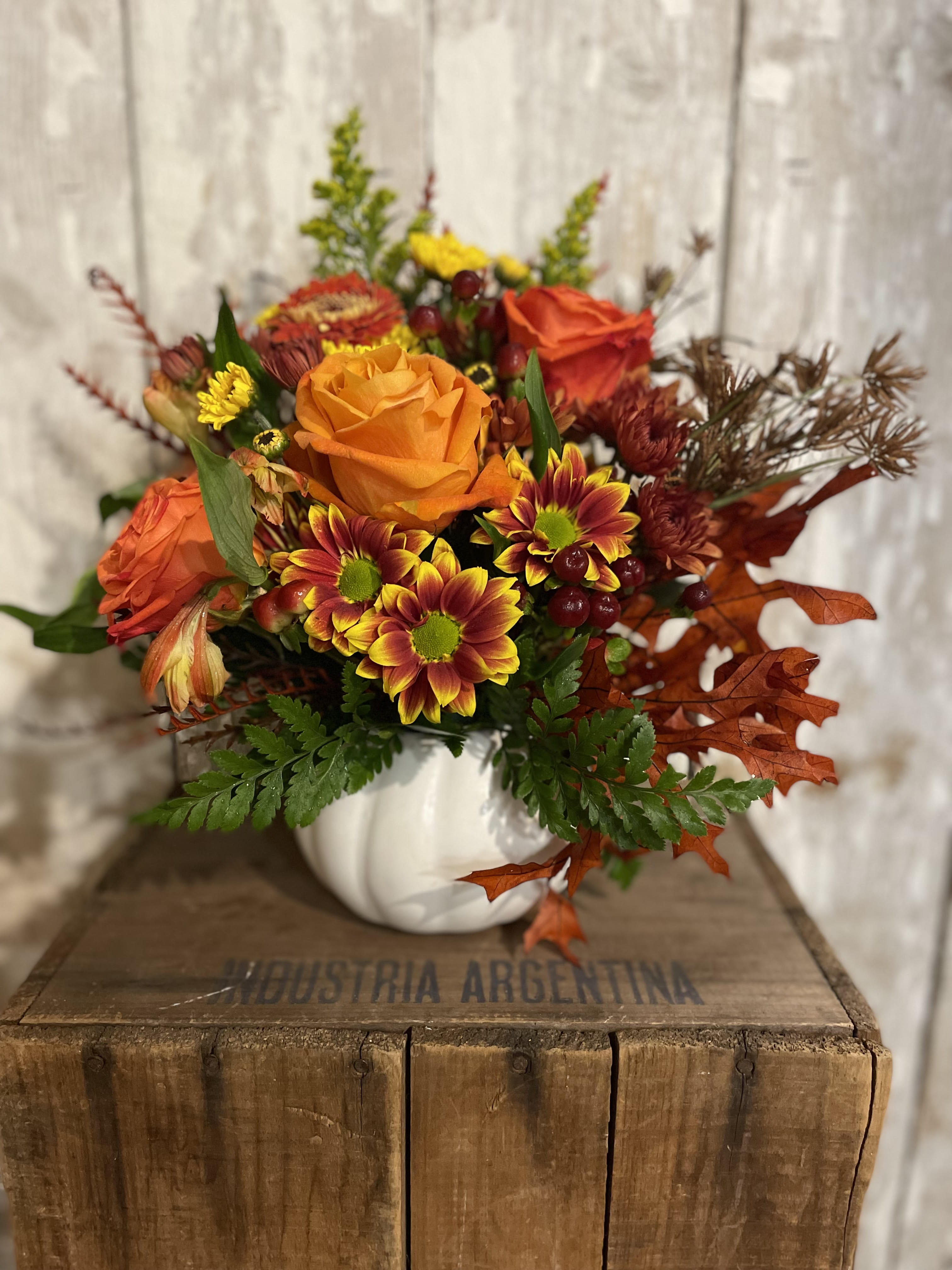 Autumn bouquet with orange roses and yellow-red chrysanthemums in a white pumpkin vase