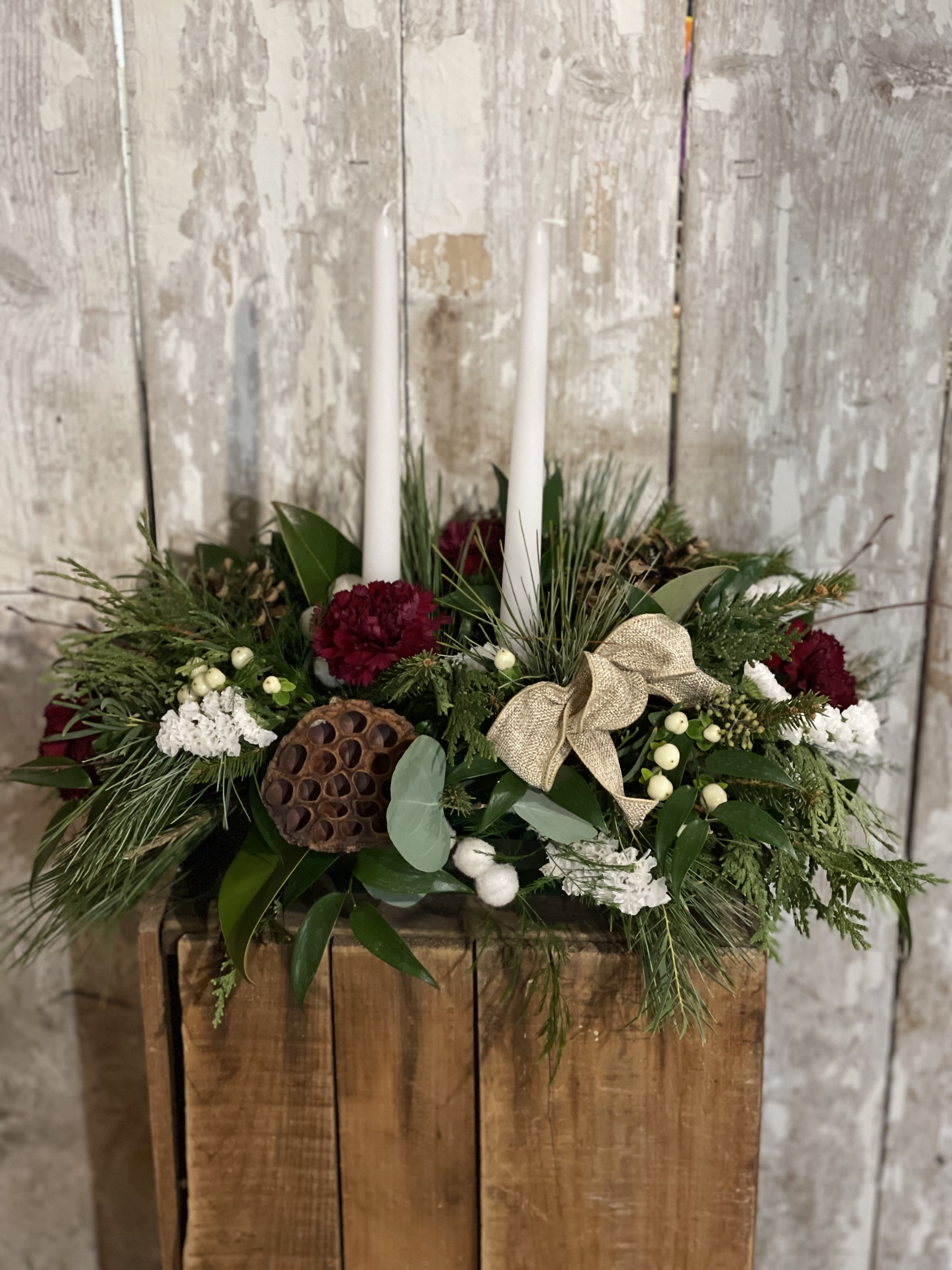 Holiday centerpiece with white candles, red flowers, and greenery in a wooden box