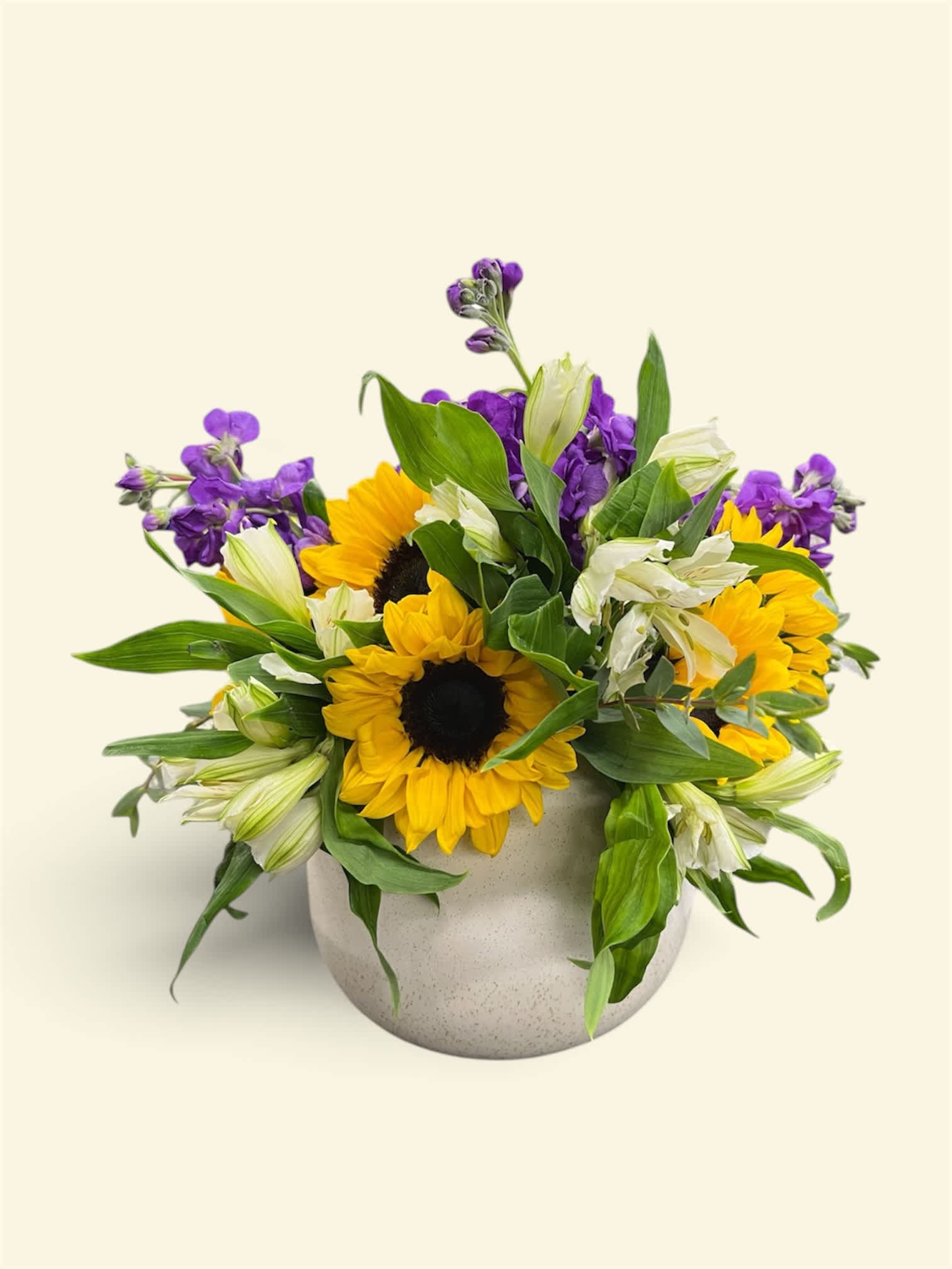 Sunflowers and purple flowers arranged in a round ceramic vase