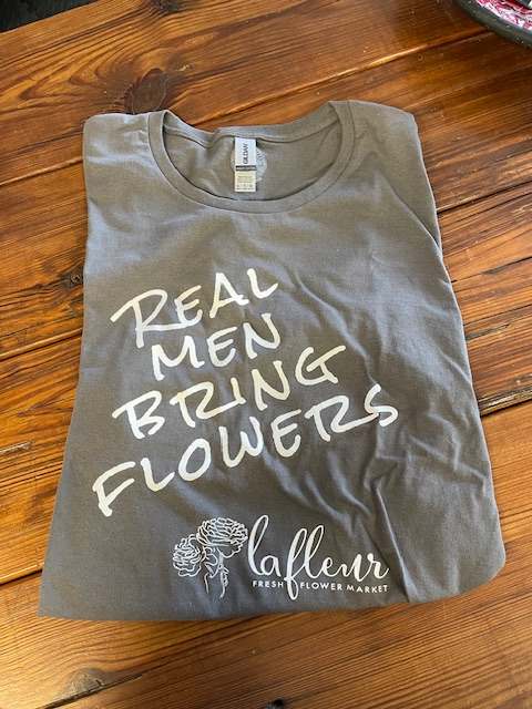 Real Men Bring Flowers T-Shirt - Reward him, remind him or encourage all to bring flowers with this fun t-shirt. Available in medium, large, and extra large.