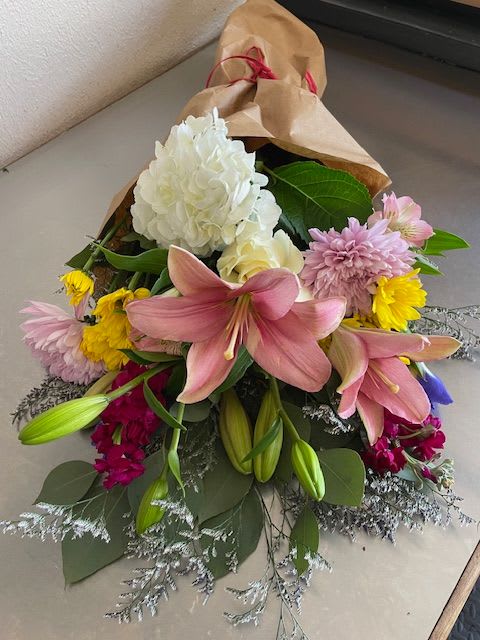 Bouquet of pink lilies, white hydrangea, and mixed blooms wrapped in brown paper